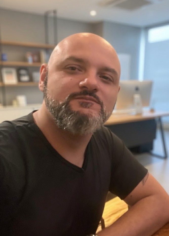 Retrato de Wilder Martins, de camiseta preta, sorrindo levemente em um escritório